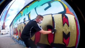 Otto Toivainen maalaamassa Totuusfoorumin nimikkograffitia Suvilahden seinälle.